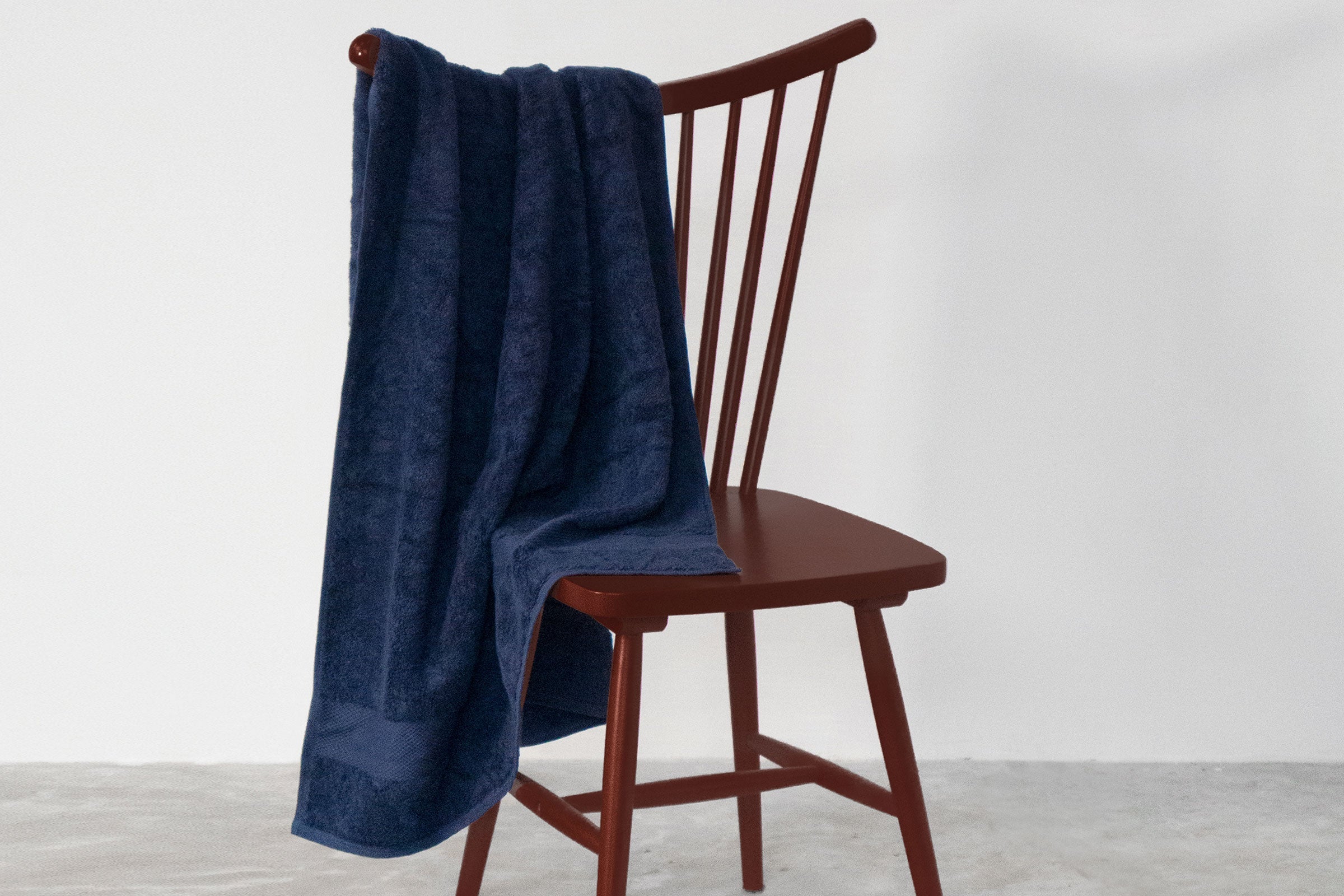 organic-cotton-bath-towel-in-navy-colour-hanging-over-a-chair-by-sojao