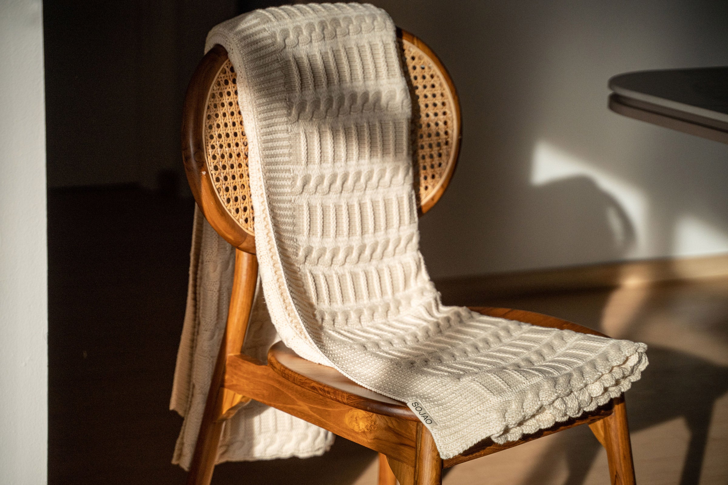organic-cotton-cable-knit-throw-in-ivory-colour-hanging-over-a-wooden-chair-by-sojao